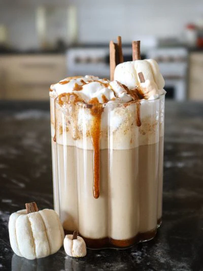 Frappuccino à la citrouille avec un sirop à la citrouille sur la crème fouettée au-dessus du verre. Deux guimauves sont au-dessus du sirop et deux autres au pied du verre.